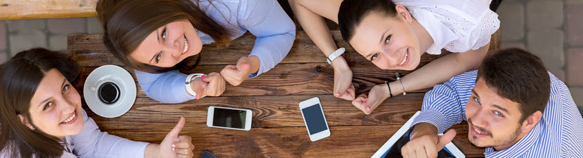 Photo of students sitting around a table with cell phones and tablet